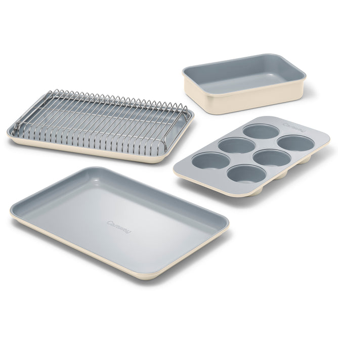 The Caraway Mini Bakeware Set w/ Storage includes four cream and gray ceramic-coated pieces—a muffin pan, baking sheet, roasting pan with rack, and rectangular cake pan—shown on a white background.