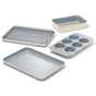 The Caraway Mini Bakeware Set w/ Storage includes four cream and gray ceramic-coated pieces—a muffin pan, baking sheet, roasting pan with rack, and rectangular cake pan—shown on a white background.