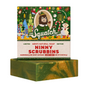 A green and yellow swirled Dr. Squatch Ninny Scrubbins Bar Soap, inspired by Buddy the Elf and made with marshmallow root extract, sits in front of its festive holiday box decorated with cheerful illustrations.