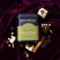 A tin of Spicewalla Deluxe Mexican Hot Chocolate sits on purple velvet, surrounded by toasted marshmallows, chocolate pieces, cinnamon sticks, cardamom pods, and chocolate chips.