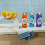 A person pours Grove Co. Hand Soap – Hydrates & Moisturizes With Every Wash from a yellow carton into a clear dispenser on a countertop, with three colorful recyclable cartons, a striped towel, and blue tiled wall in the background.