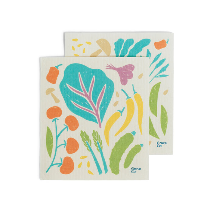 These Grove Co. Swedish Dishcloths—lasting up to 6 months—feature colorful veggies like tomatoes, peppers, carrots, asparagus, and greens on white. Sustainable and reusable kitchen towels with the Grove Co. logo in the corner.