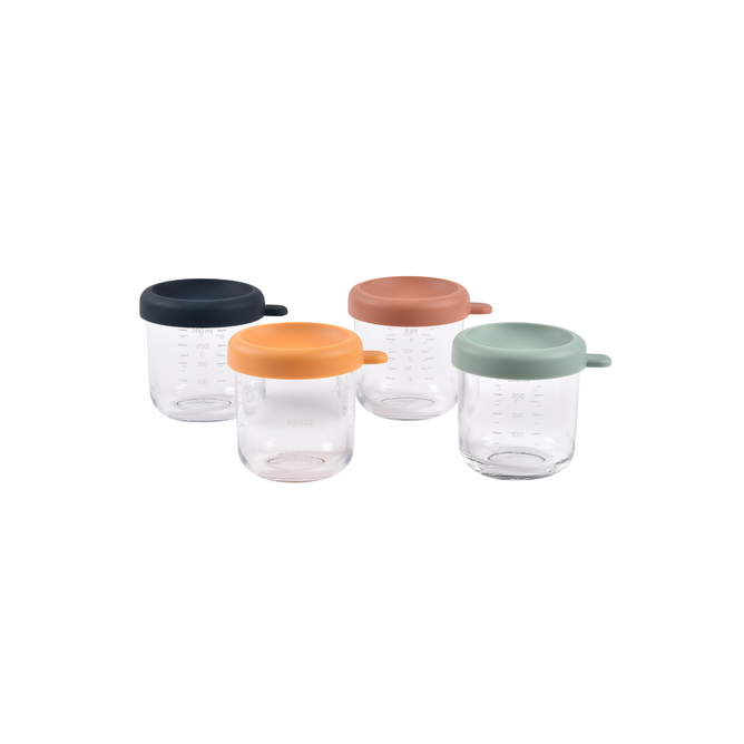 The BEABA Glass Baby Food Jars set includes four clear jars with silicone lids in navy blue, orange, pink, and mint green, each with a small handle—ideal for storing or serving homemade baby food.