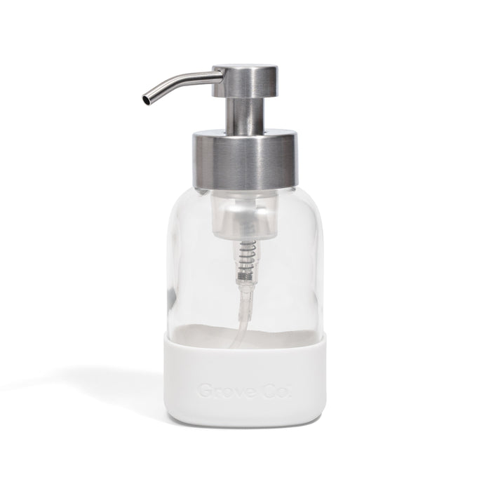 A Grove Co. Foaming Hand Soap Dispenser with a white silicone sleeve, featuring a clear glass body and stainless steel pump, designed with a refillable system to help reduce plastic waste, photographed on a plain white background.
