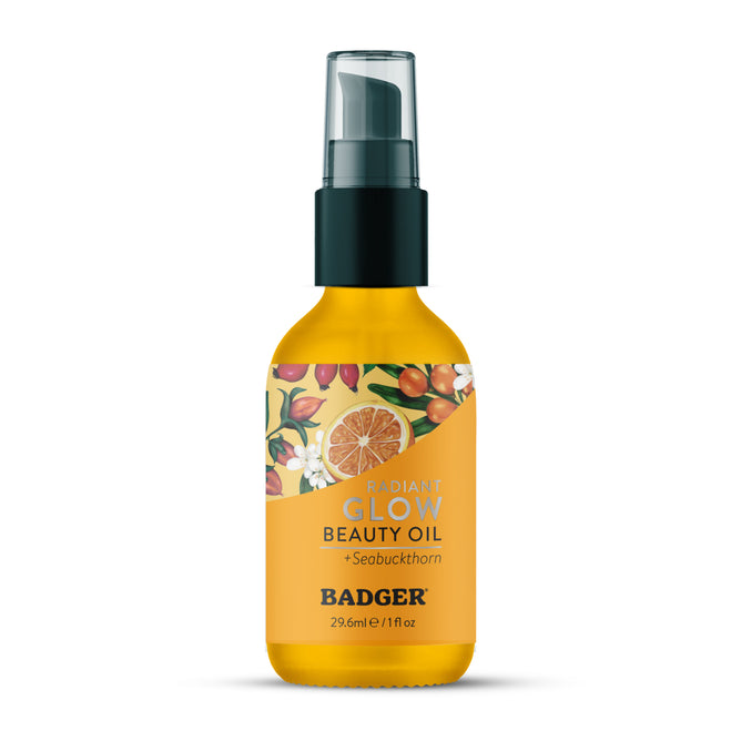A 29.6 ml (1 fl oz) bottle of Badger Balm Seabuckthorn Glow Beauty Oil features a biocompatible oil formula, ideal for organic skincare routines. The yellow-orange label is adorned with floral and fruit illustrations, and the bottle includes a convenient pump dispenser.