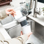 A person rinses an NSF certified Pure XP Water Filter Pitcher cartridge from Epic Water Filters USA over a kitchen sink, holding the filter in one hand and a clear container in the other, preparing it for use in their water filter pitcher to ensure effective reduction of fluoride, PFAS, and parasites.