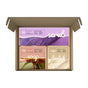 An open cardboard box from Soapymania displays a Body Care Set with three bath products: a purple sugar scrub cubes box, a pink exfoliating bar soap box, and a beige loofah box, each featuring vibrant images and clear labels.