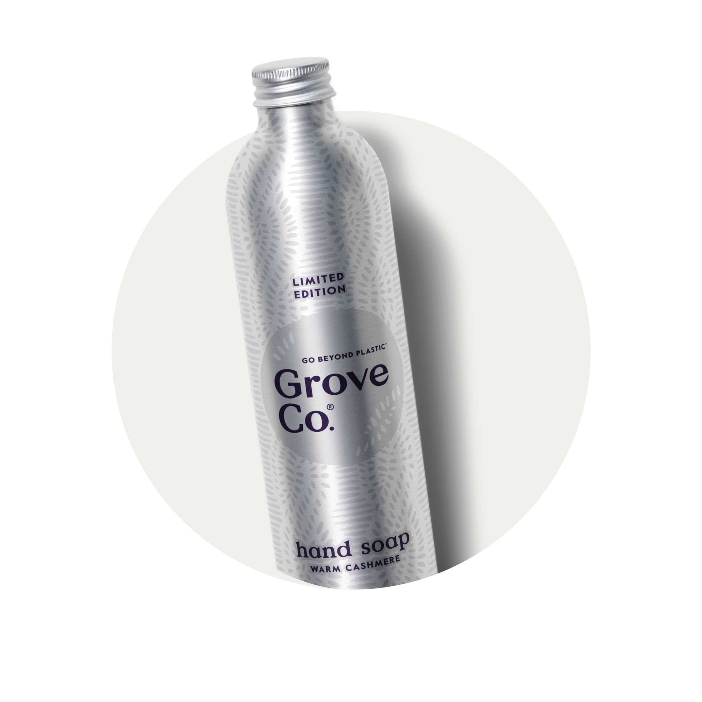 A silver metal bottle of Grove Co. Limited Edition hand soap in the Warm Cashmere scent, featuring a patterned surface and a screw-top lid, positioned diagonally on a light background.