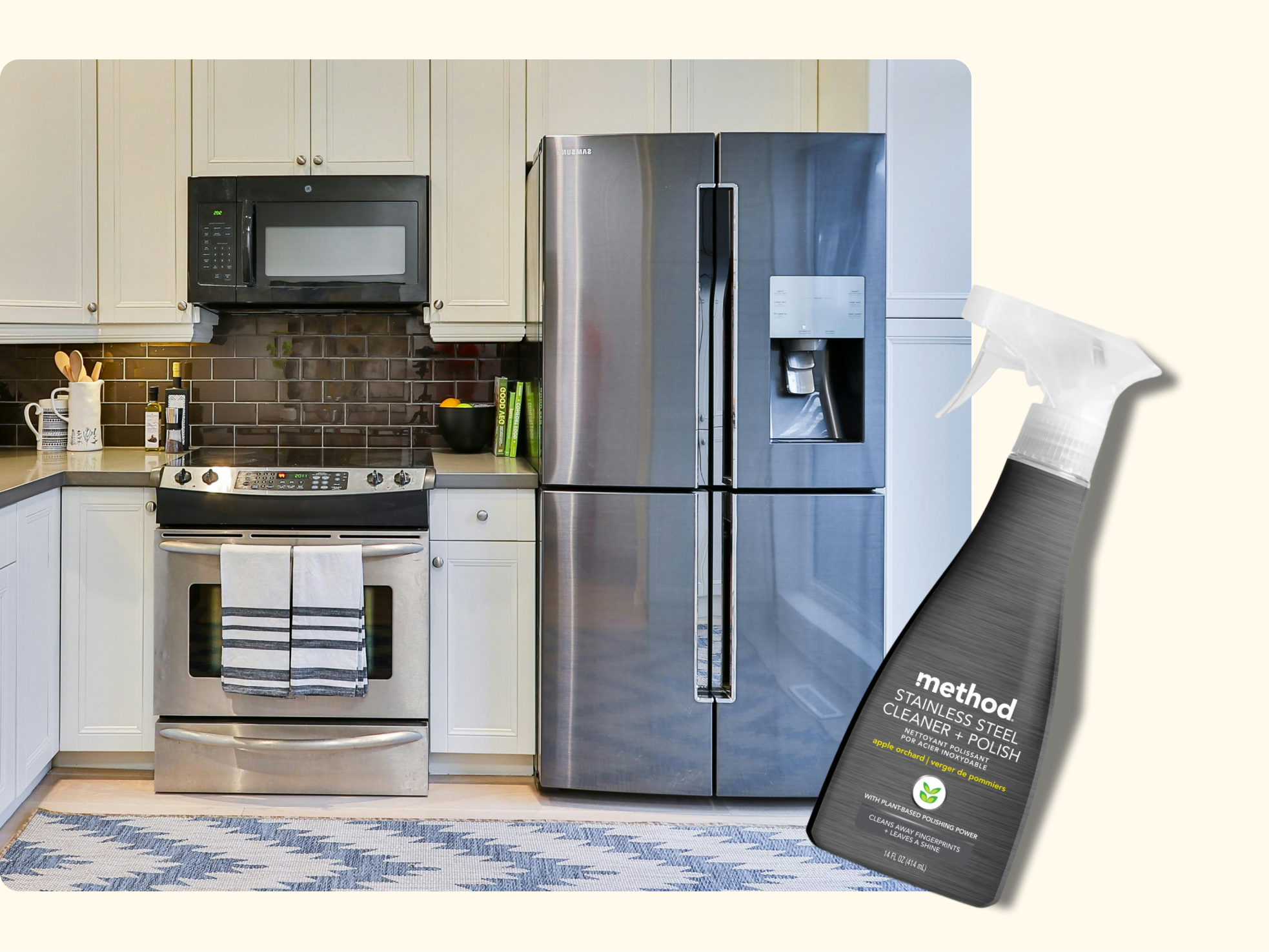 A modern kitchen with white cabinets, stainless steel appliances, and a chevron rug. In the foreground, a spray bottle of Method stainless steel cleaner is shown.