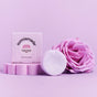 A plastic-free Strengthening Conditioner Bar - Super Bloom by Sunniemade, enriched with nourishing rosehip oil, is displayed next to its box labeled with the brand and product name, accompanied by a vibrant pink rose—all artfully arranged on a pink background.