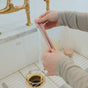 A person rinses an Esembly Baby Reusable Silicone Sipper Straw from the 4-pack with storage pouch made from upcycled materials under a kitchen faucet, highlighting their eco-friendly commitment to sustainable sipping.