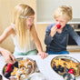 Two children enjoy breakfast from Ahimsa’s Purposeful Plate, smiling as they eat star-shaped waffles with powdered sugar, blackberries, and raspberries. The boy bites into a strawberry while the girl laughs, creating a joyful mealtime moment.