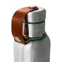 A close-up of the Black + Blum Insulated Water Bottle featuring a green silicone ring near the cap and a brown leather strap secured with a metal snap button.
