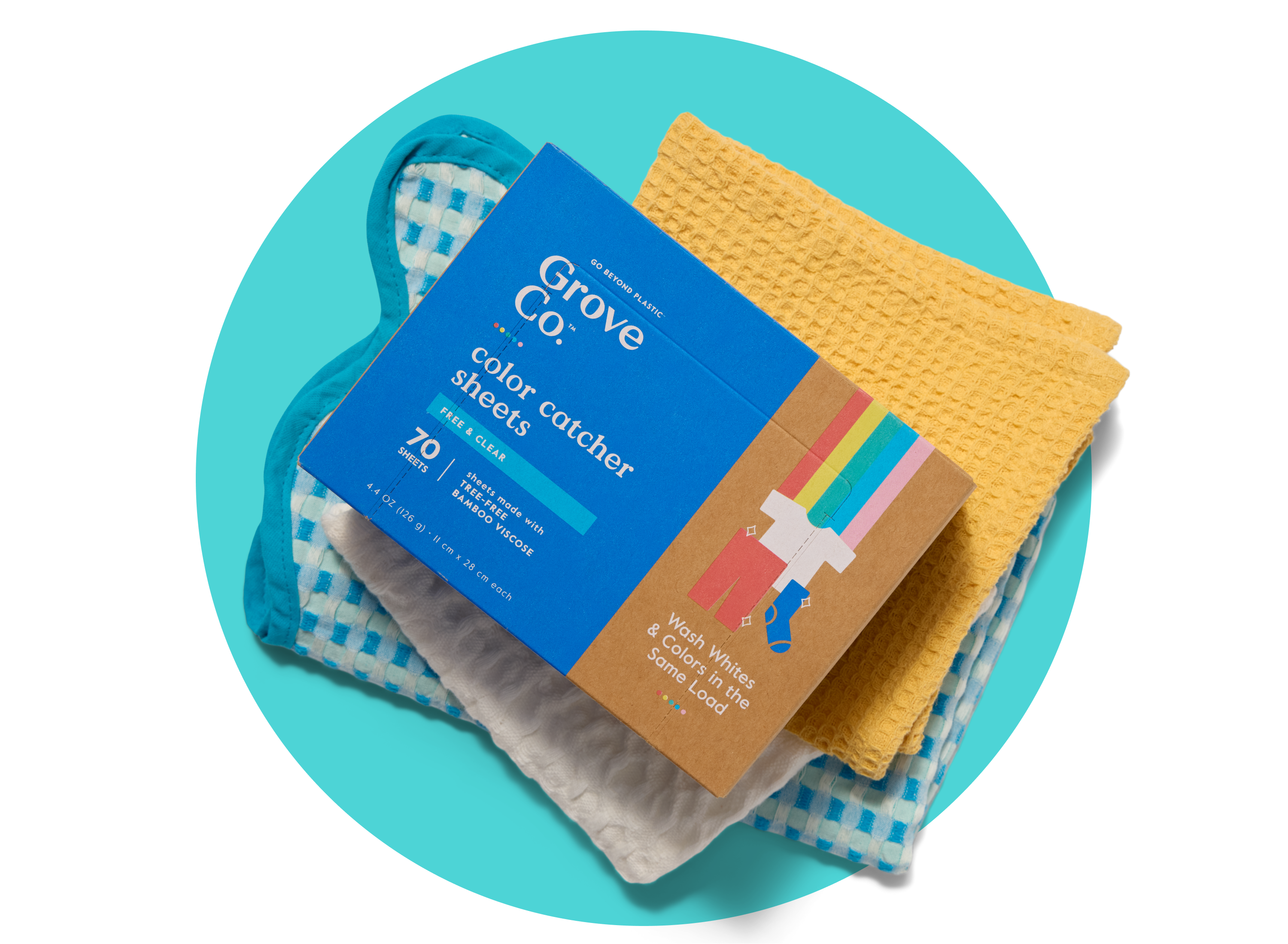 A box of Grove Co. color catcher sheets is stacked on top of folded yellow and white towels and a blue-and-white checkered oven mitt, all placed on a turquoise circular background.