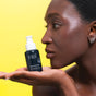 A person with radiant skin holds a FRÉ Skincare RECOVER ME Restorative Night Cream bottle on their palm against a bright yellow background, highlighting the product.
