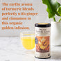 A tin of The Republic of Tea Organic Turmeric Ginger Green Tea rests on a marble counter beside a mug of golden tea and a vase with green leaves. Text highlights the blend’s earthy aroma with ginger, turmeric, and cinnamon notes.