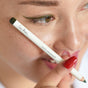A person with red nails holds the Ere Perez Jojoba Eye Pencil near their face, showcasing green-winged eyeliner—ideal for sensitive skin—on their closed eye.