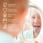 A young child sticks out their tongue while looking in a mirror. Text on the left lists benefits: Ahimsa Mindful Mealtime Set—pediatrician-designed, protects from bacterial growth, eco-friendly, dishwasher-safe, and free of harmful chemicals.