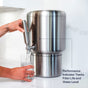 A person dispenses water from a Rorra Countertop System, a modern stainless steel water filtration system by Rorra, into a glass. Text reads: NSF tested; Performance Indicator tracks filter life and water level, and helps remove lead.