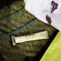 A tube of Sunniemade Healing Lip Balm – Hello Aloe, enriched with soothing aloe vera, is placed on a striped green and blue fabric, with a white cloth embroidered with butterflies close by.