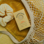 A yellow towel, mesh bag, scrunchie, and a box of Sunniemade Moisturizing Hand & Body Bar Soap – Main Squeeze are arranged together, creating a cozy, spa-like setting with warm yellow tones and a touch of natural body care.