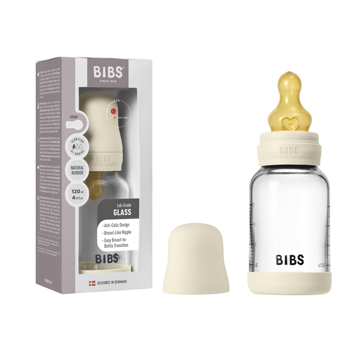 The BIBS Glass Baby Bottle with Natural Rubber Nipple Complete Set in beige rests beside its box showing anti-colic features. The clear bottle has measurement markings and the BIBS logo for convenient, easy use.