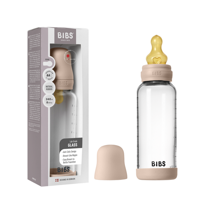 A BIBS Glass Baby Bottle with Natural Rubber Nipple Set – Medium Flow 2+ Months is shown with a beige lid and cap next to its upright packaging, highlighting product details and branding.