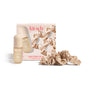 Beige satin scrunchies and two Kitsch hair care products (vanilla and pink grapefruit) are arranged on a white background in front of the Happy Holiday Hair Set box, which features pink text.