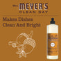Mrs. Meyers Dish Soap in Acorn Spice, a fall-scented soap, is displayed on a brown background with acorn and leaf designs. Text: Makes Dishes Clean And Bright.