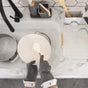 Wearing Full Circle High & Dry Cleaning Gloves for hot water protection, a person washes a white plate in a marble sink, with soapy water nearby and clean glasses drying, plus kitchen tools and a sponge holder on the counter.