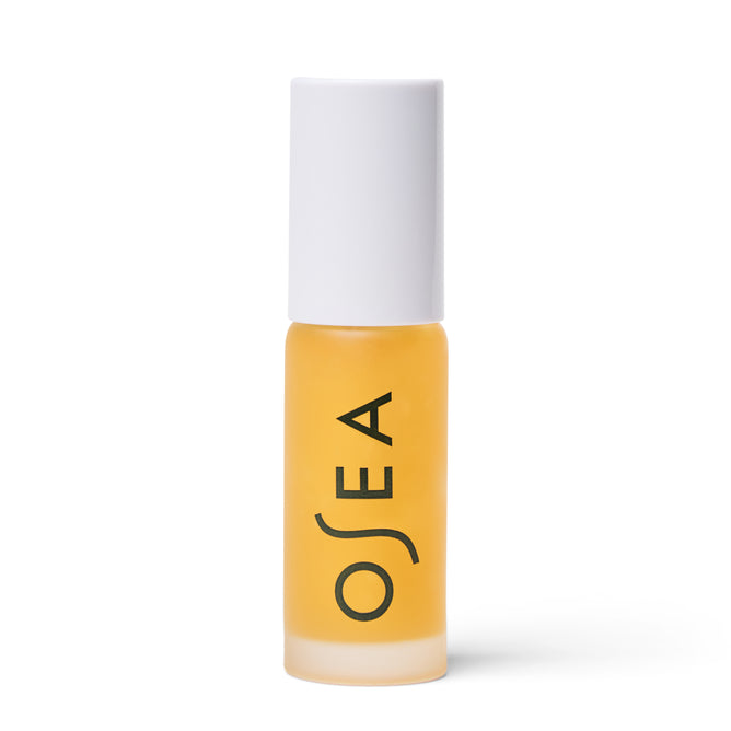 A small frosted glass bottle with yellow liquid, a white cap, and “OSEA” printed vertically in black holds the brand’s Hyaluronic Lip Oil Booster.