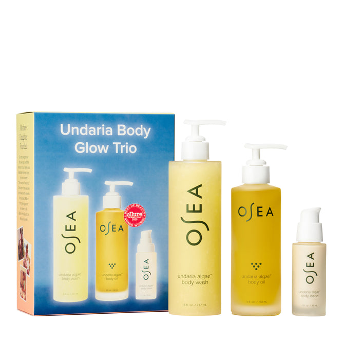 The OSEA Undaria Body Glow Trio features a branded box and three yellow bottles—a body wash and Undaria Algae Body Oil with pumps, plus a serum with a white cap—all arranged in front of the packaging.
