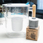 A clear Pure XP Water Filter Pitcher from Epic Water Filters USA sits on a counter beside a replacement filter cartridge and its packaging, highlighting its ability to reduce fluoride, PFAS, and parasites. A couch and window are visible in the blurred background.