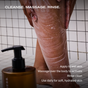 In a tiled shower, someone massages Ember Wellness Hydrating Body Cleanser—an oil-to-milk formula—onto their lower leg, with its pump bottle in the foreground and text instructions for cleansing, massaging, and rinsing to boost skin hydration.