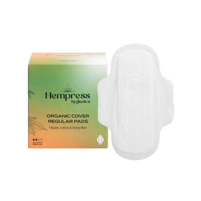 A box of Hempress Hygienics Organic Cover Regular Pads is shown next to a single white sanitary pad. The box is green and orange, labeled as organic, biodegradable, and plant-based.