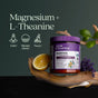 A container of New Chapter Magnesium + L-Theanine Powder sits on a wooden branch with a lemon slice, lavender, and green leaves. Icons showcase benefits for calm, mental clarity, and focus.
