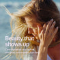 A blonde woman stands by the beach, touching her hair. Text reads: Beauty that shows up. New Chapter Hair & Nail Defense Capsules - with Biotin for Healthy Hair Growth support effortless routines and lasting strength.