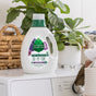 A bottle of Seventh Generation Liquid Laundry Detergent rests on a white washing machine, surrounded by green potted plants and a wicker basket in a bright, clean laundry room.
