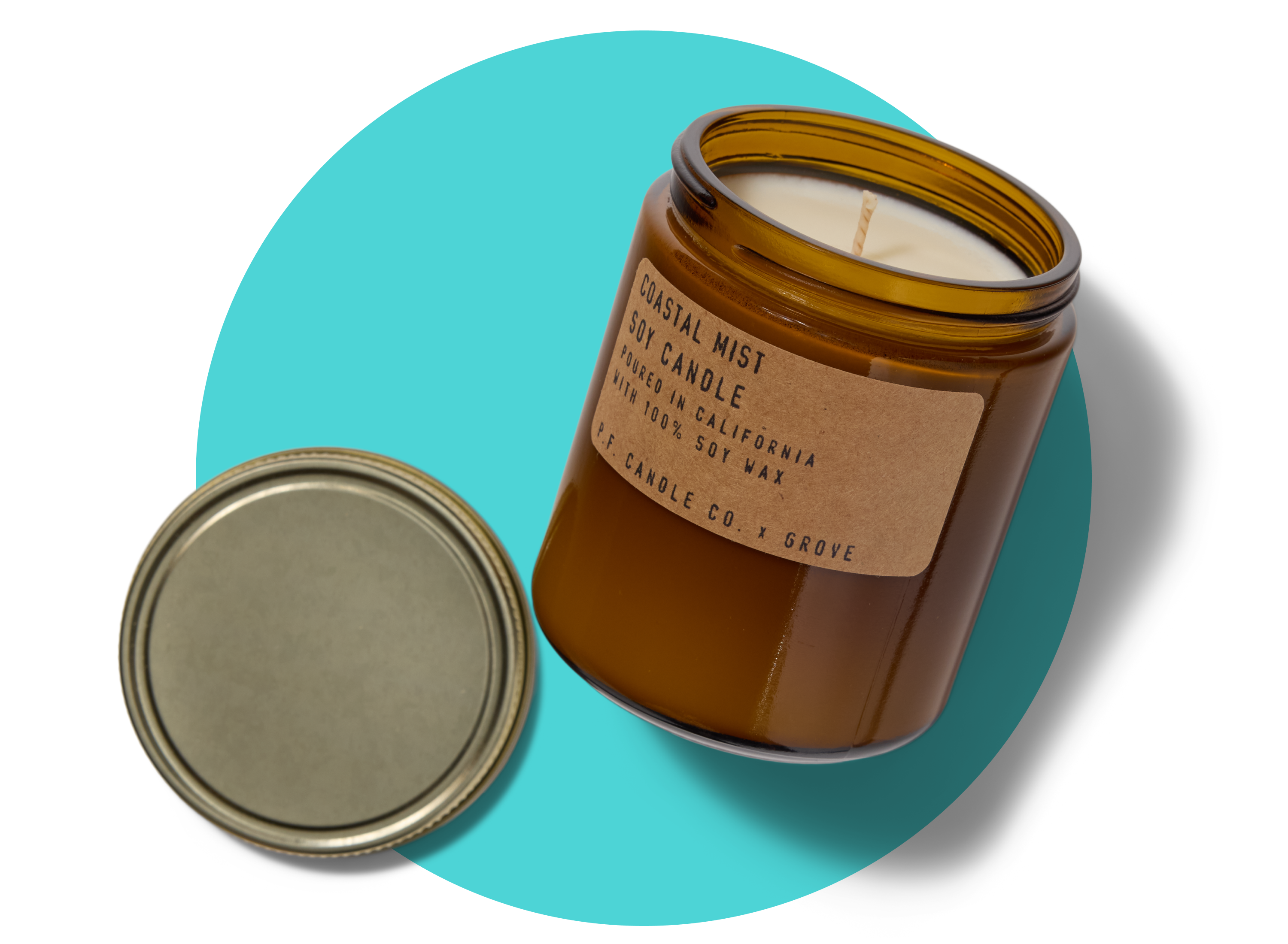A brown glass jar candle labeled Coastal Mist Soy Candle with its metal lid off, placed beside it on a white background with a blue circle accent behind the candle.