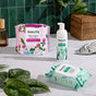 HoneyPot’s Cooling Intimate Wash - Herbal Infusion is displayed on a countertop alongside organic cotton cover pads and cleansing wipes, with green plants, a wicker basket, and a green tiled wall in the background.