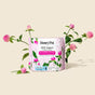 A pink package of HoneyPot Peri-menopause All Day/All Night Pads - Harmonizing Herbal Infusion rests among pink clover flowers and green leaves on a beige background.