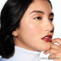 A woman with smooth skin, glossy lips, and neat brows poses in a white turtleneck, touching her chin. Her lips glow with RMS Beauty Lip2cheek. The text CRYSTAL SLIPPER appears in the bottom right corner.