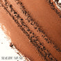 A close-up of bronze-colored ReDimension Hydra Bronzer by RMS Beauty, artistically spread in textured streaks across a surface. The words RMS Beauty appear in the lower left corner.