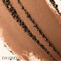 Close-up of loose brown powder, likely RMS Beauty’s ReDimension Hydra Bronzer, with three darker diagonal lines; TAN LINES is shown in the bottom left corner.