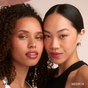 Two women pose closely—one with deep brown skin and curls, the other with medium skin and straight black hair—both glowing in natural makeup set by RMS Beauty Hydra Setting Powder. “DEEP” and “MEDIUM” shades feature in the lower corners.