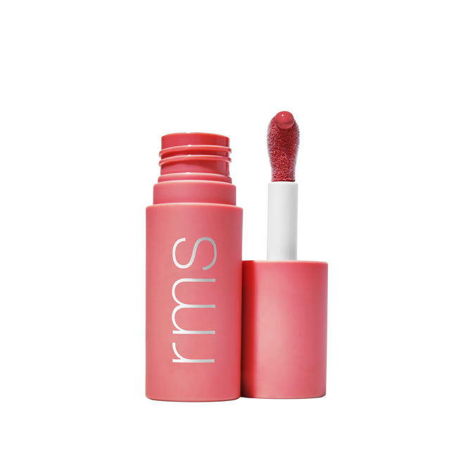 A pink tube of RMS Beauty Legendary Lip Oil with the wand applicator upright beside it, showcasing its vibrant color and hydrating formula with Organic Jojoba Oil on the sponge tip.