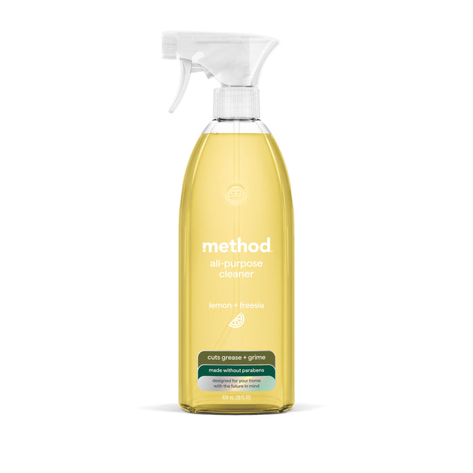 A clear spray bottle of method All Purpose Cleaner, lemon + freesia scent, holds yellow liquid. The label notes natural cleaning power for a streak-free finish and that it cuts grease and grime without parabens.