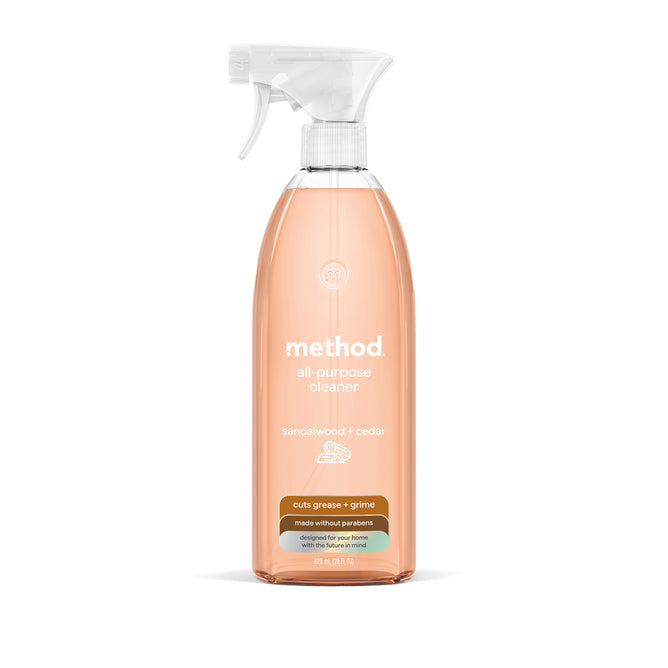 A clear spray bottle of method All Purpose Cleaner in sandalwood + cedar scent, with a white nozzle and peach liquid. The label promotes natural grease-fighting power for a streak-free finish and contains no parabens.