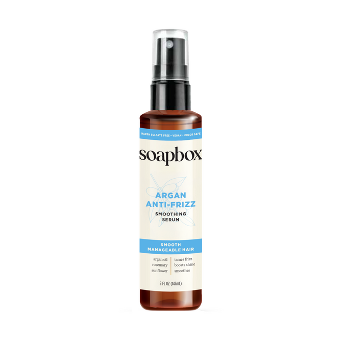 A brown bottle of Soapbox Argan Anti-Frizz Smoothing Serum features a black pump and white label. This 5 fl oz (148 mL) serum, infused with argan oil, flaxseed, and sunflower, is designed for smooth, manageable, shiny hair.