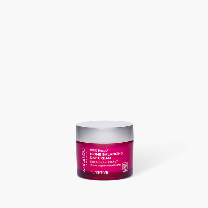 A small, translucent magenta jar of Andalou 1000 Roses Biome Balancing Day Cream with a silver lid.